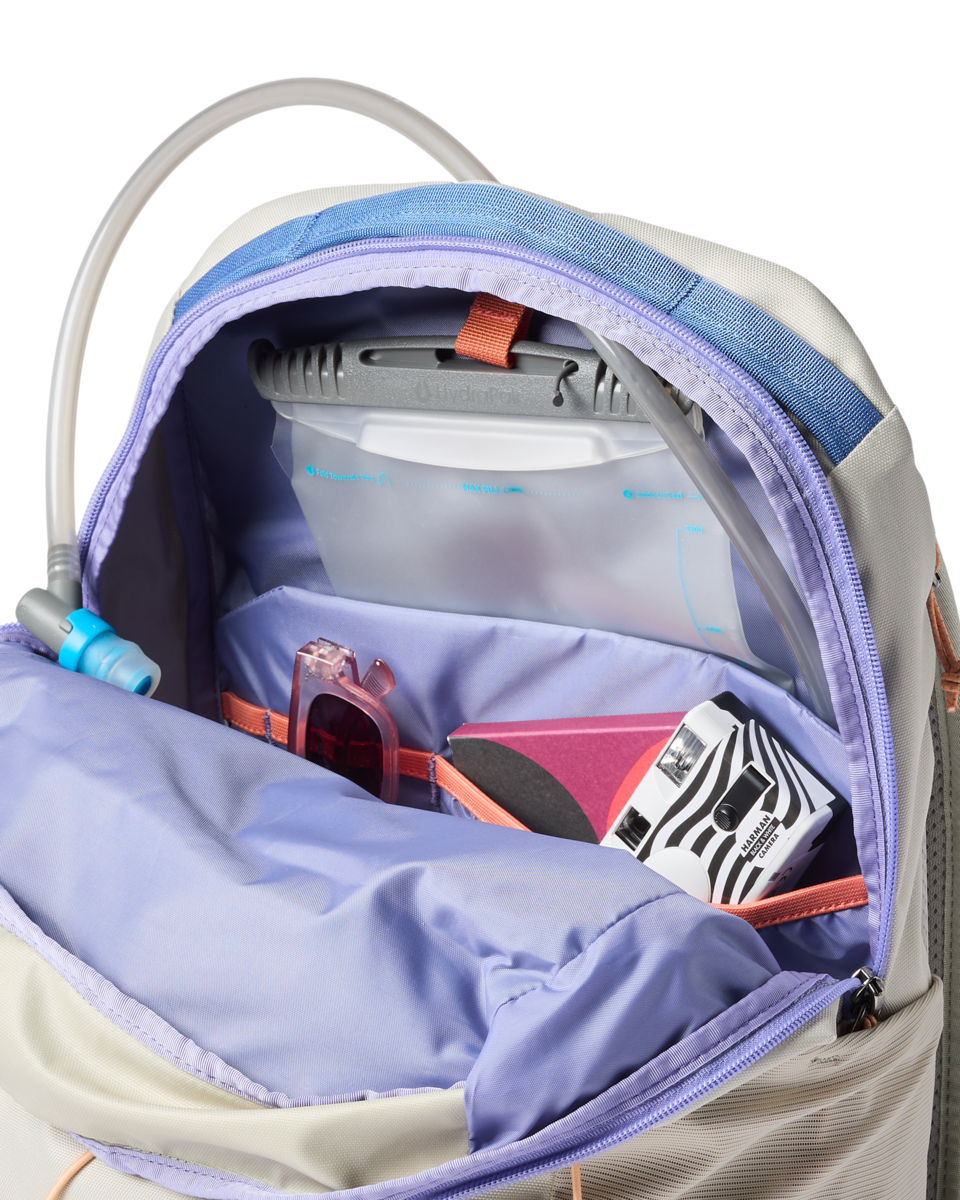Light colored backpack opened showing interior compartments with laptop sleeve and organized pockets