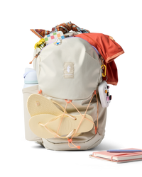 Light gray daypack with orange accents, flip-flops attached, filled with colorful items on white background