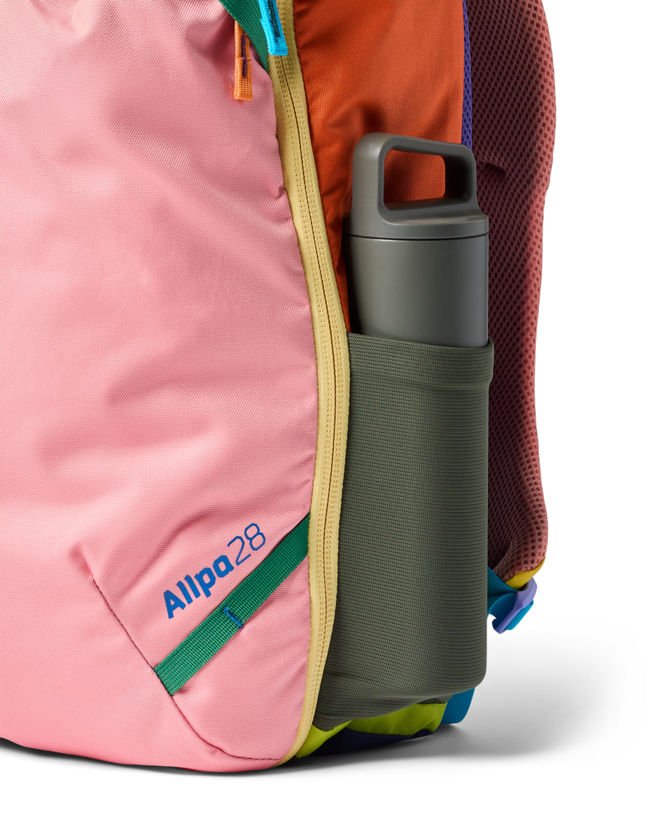 Multicolored travel backpack with water bottle in side pocket, showing various bright fabric panels