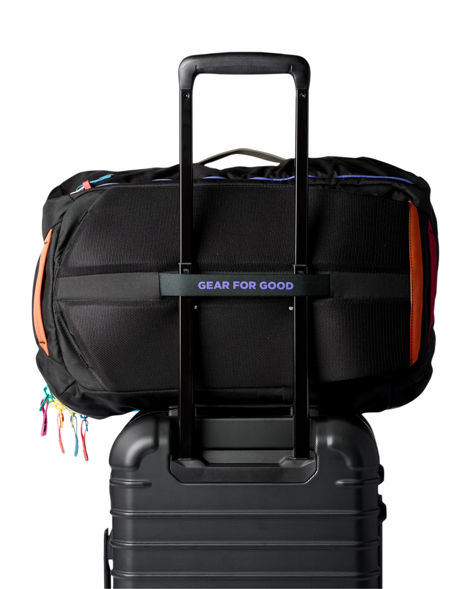 Black travel backpack with colorful zipper accents attached to rolling luggage handle
