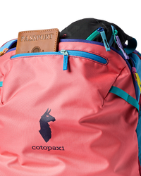 Multicolored travel backpack with passport in front pocket, showing coral pink and teal panels