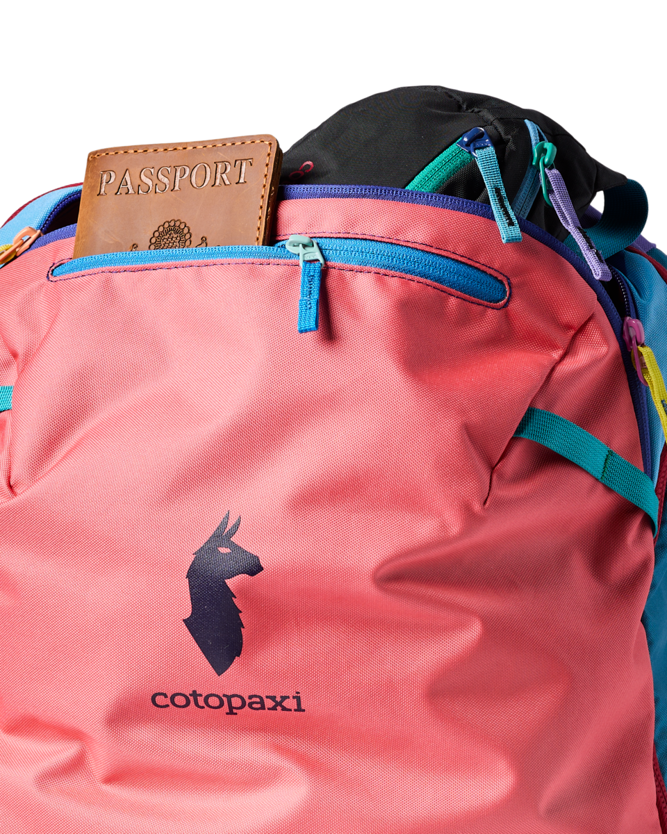 Multicolored travel backpack with passport in front pocket, showing coral pink and teal panels