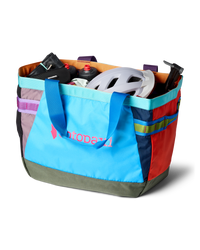 Large multicolored patchwork tote bag filled with cycling gear including helmet and water bottles