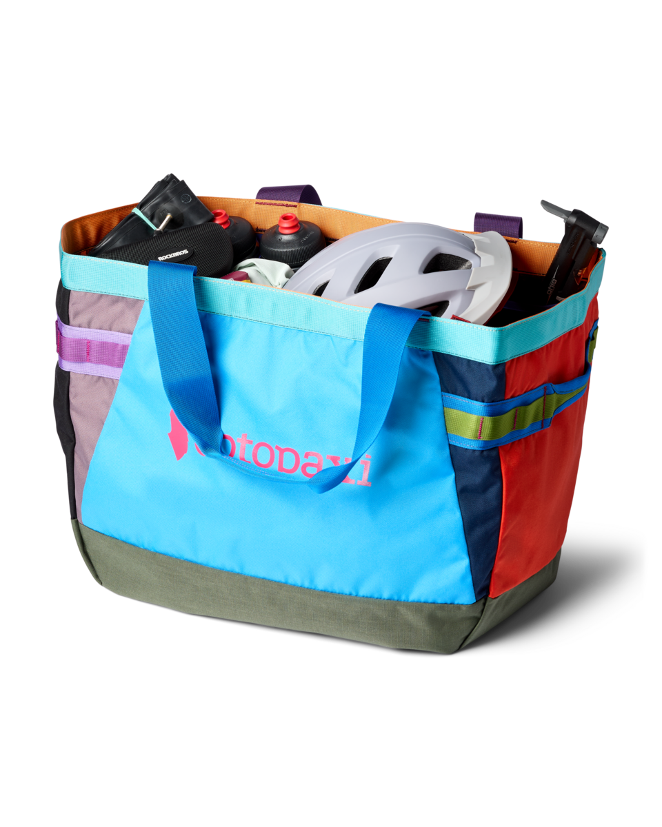 Large multicolored patchwork tote bag filled with cycling gear including helmet and water bottles