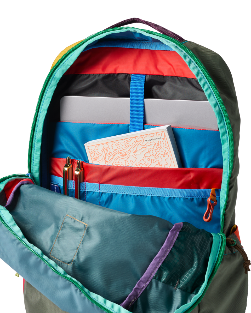 Open backpack interior detail showing multiple compartments, laptop sleeve, pens, and a book