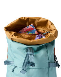 Open roll-top daypack in teal with mustard lining, showing interior zipper pocket with snacks