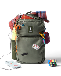 Olive green backpack with multiple compartments, accessories attached, and personal items displayed around it