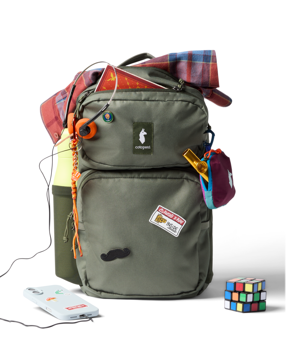 Olive green backpack with multiple compartments, accessories attached, and personal items displayed around it