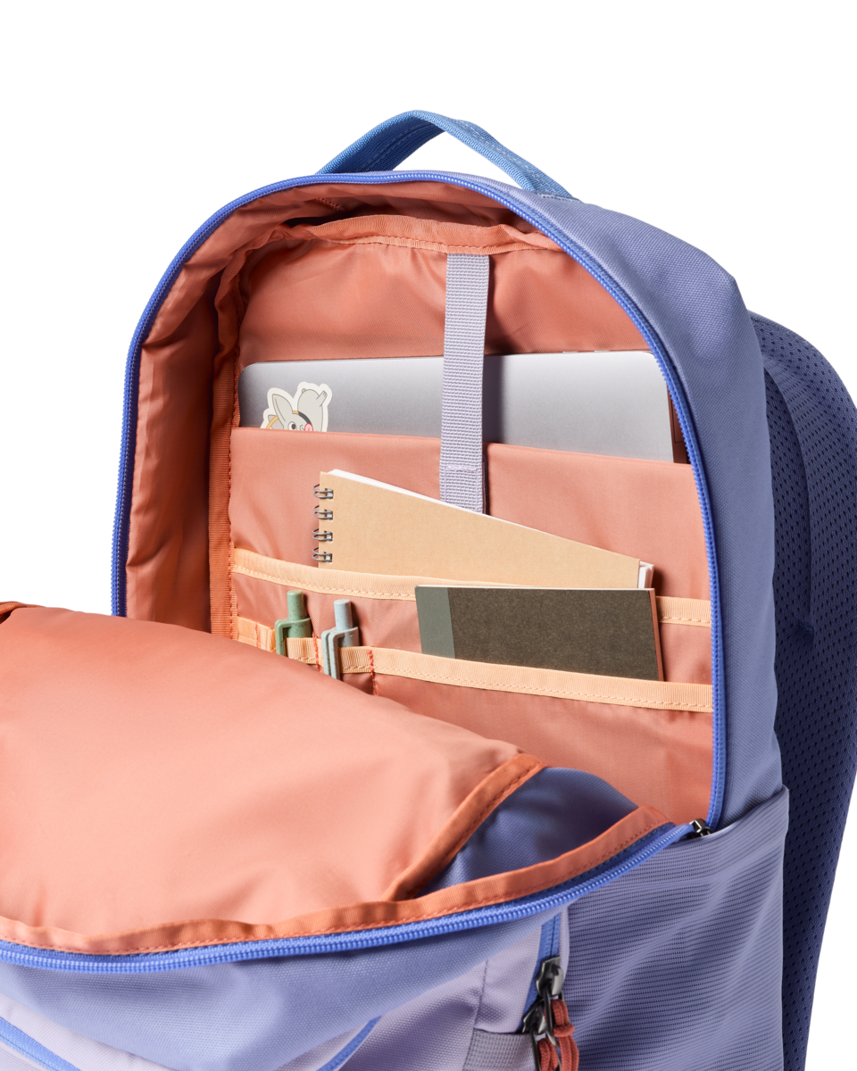 Open backpack showing interior compartments with coral lining and organizational pockets containing notebook and supplies