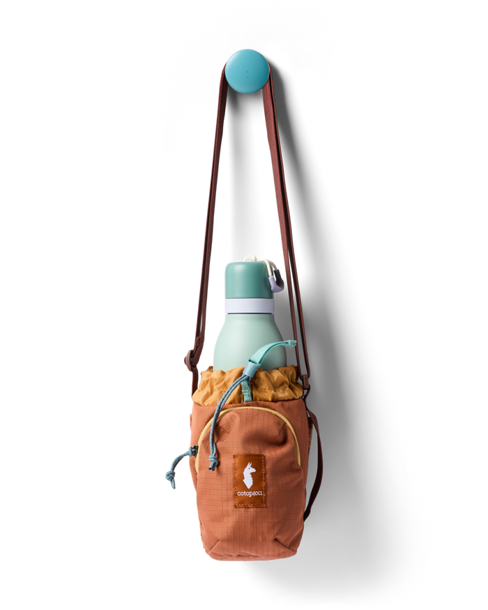 Water bottle sling bag with drawstring top holding a mint green bottle, hung on a wall hook