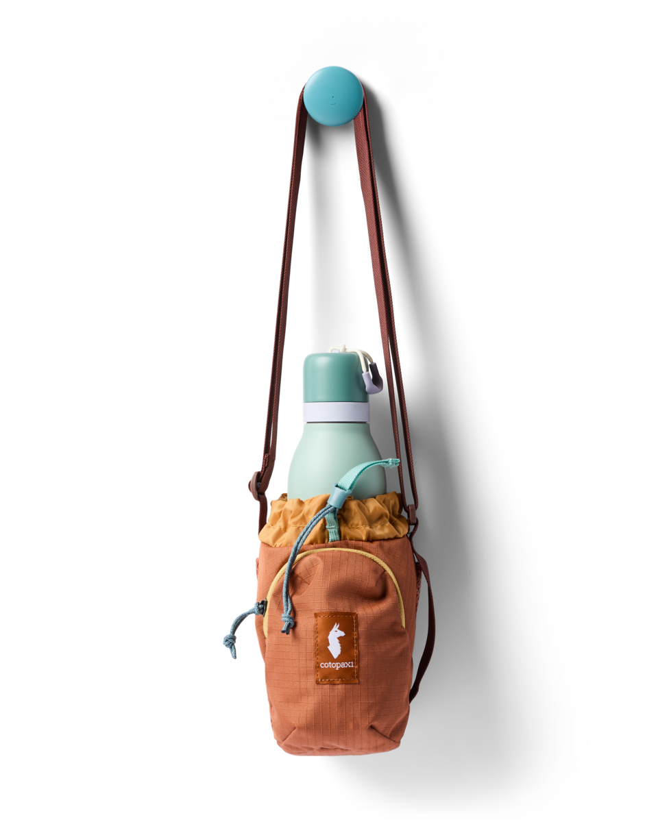 Water bottle sling bag with drawstring top holding a mint green bottle, hung on a wall hook