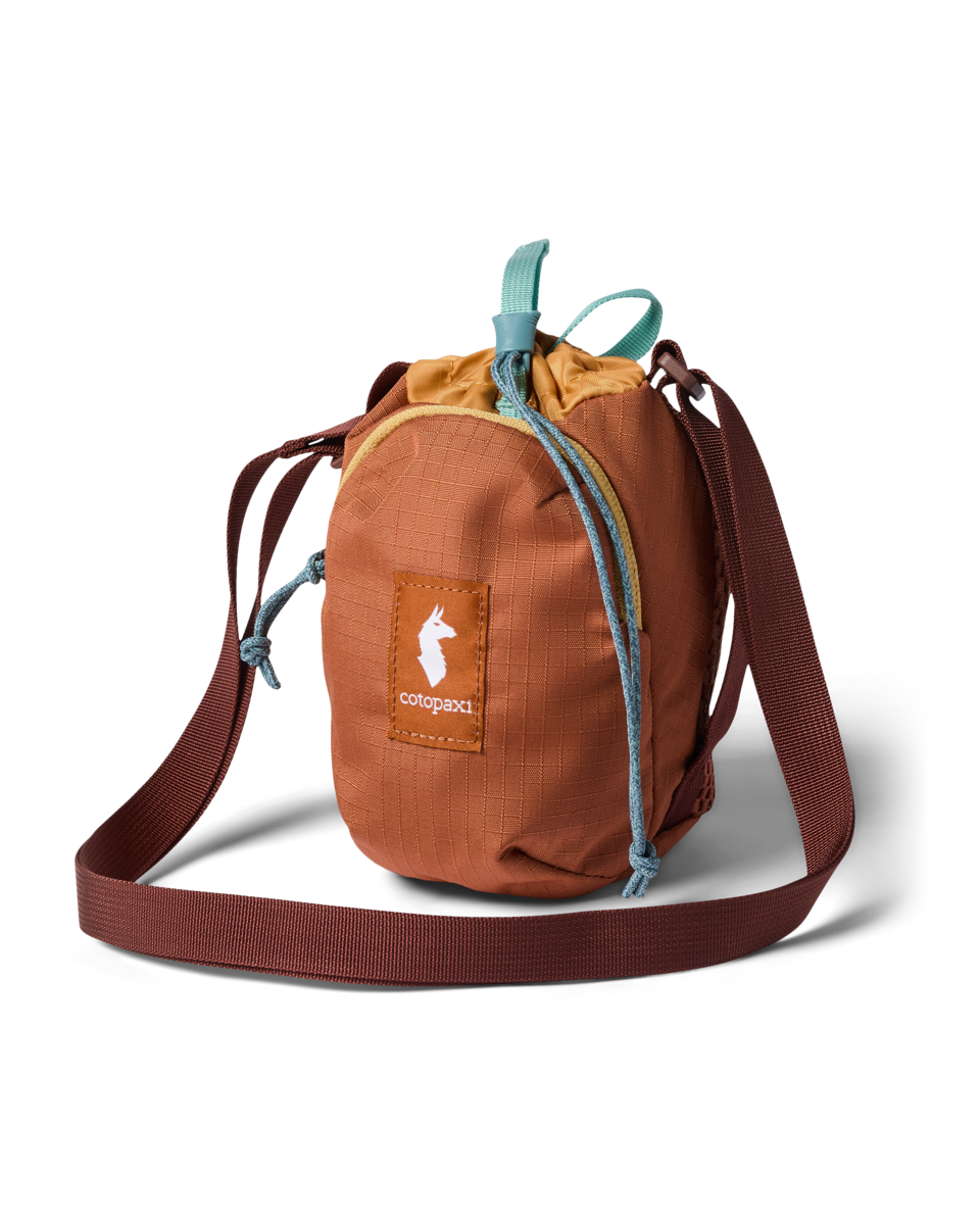 Small cylindrical drawstring crossbody sling bag with ripstop fabric, teal cord pulls, and burgundy shoulder strap