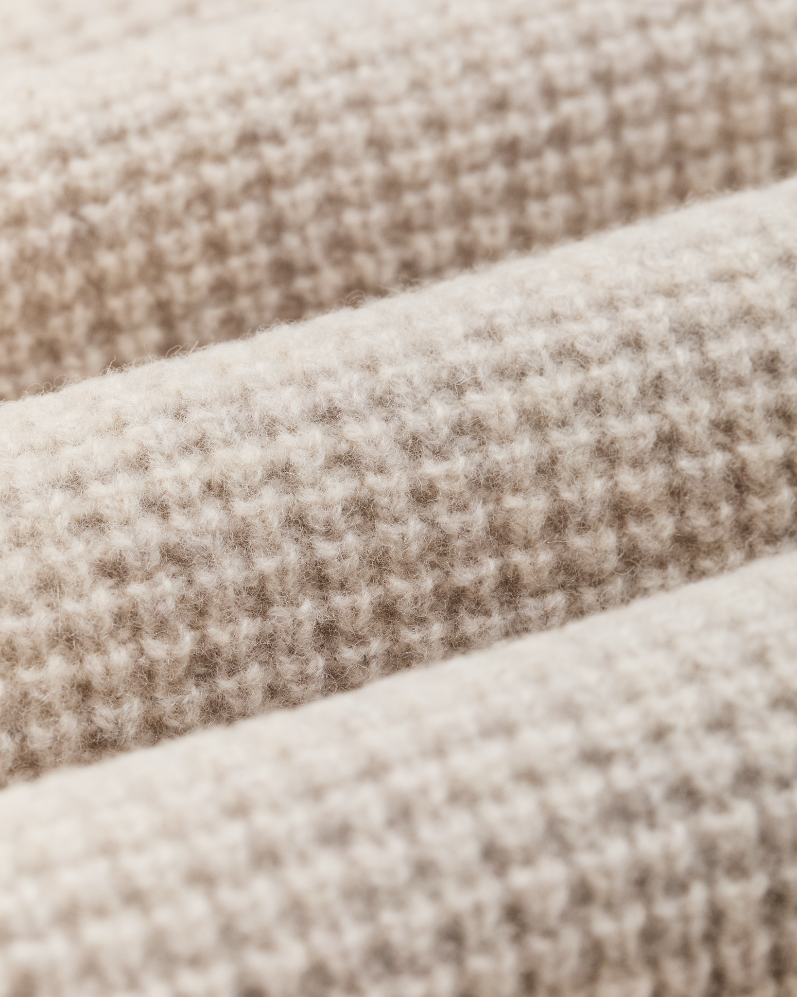 Close-up detail of waffle knit wool fabric in soft off-white heathered texture, showing stitch pattern
