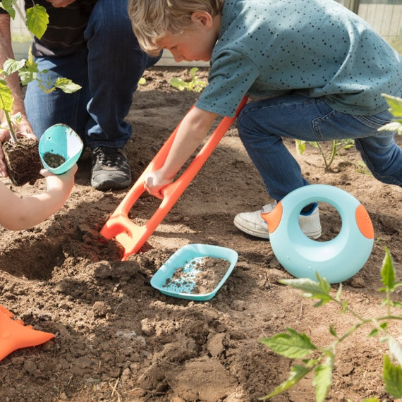 Children using turquoise sand and beach toys including shovel and watering can in garden