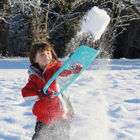 Child playing with turquoise snow shovel toy in snowy outdoor setting