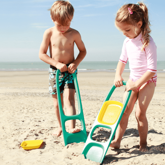 Children using teal and yellow sand scooping tool on beach