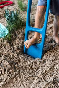 Blue digging tool being used by child's foot in sandy dirt outdoor play area