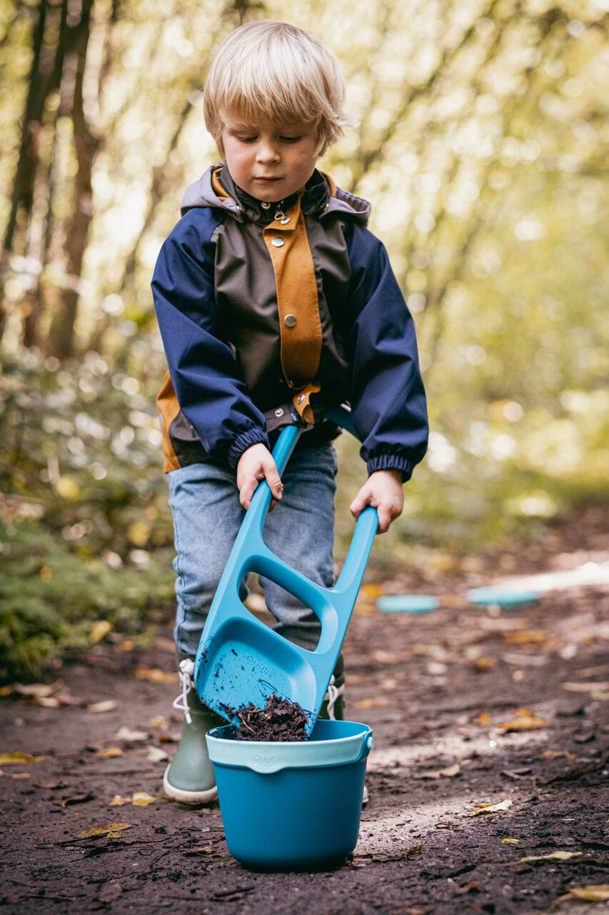 Child using blue sand scooper and bucket set outdoors on path
