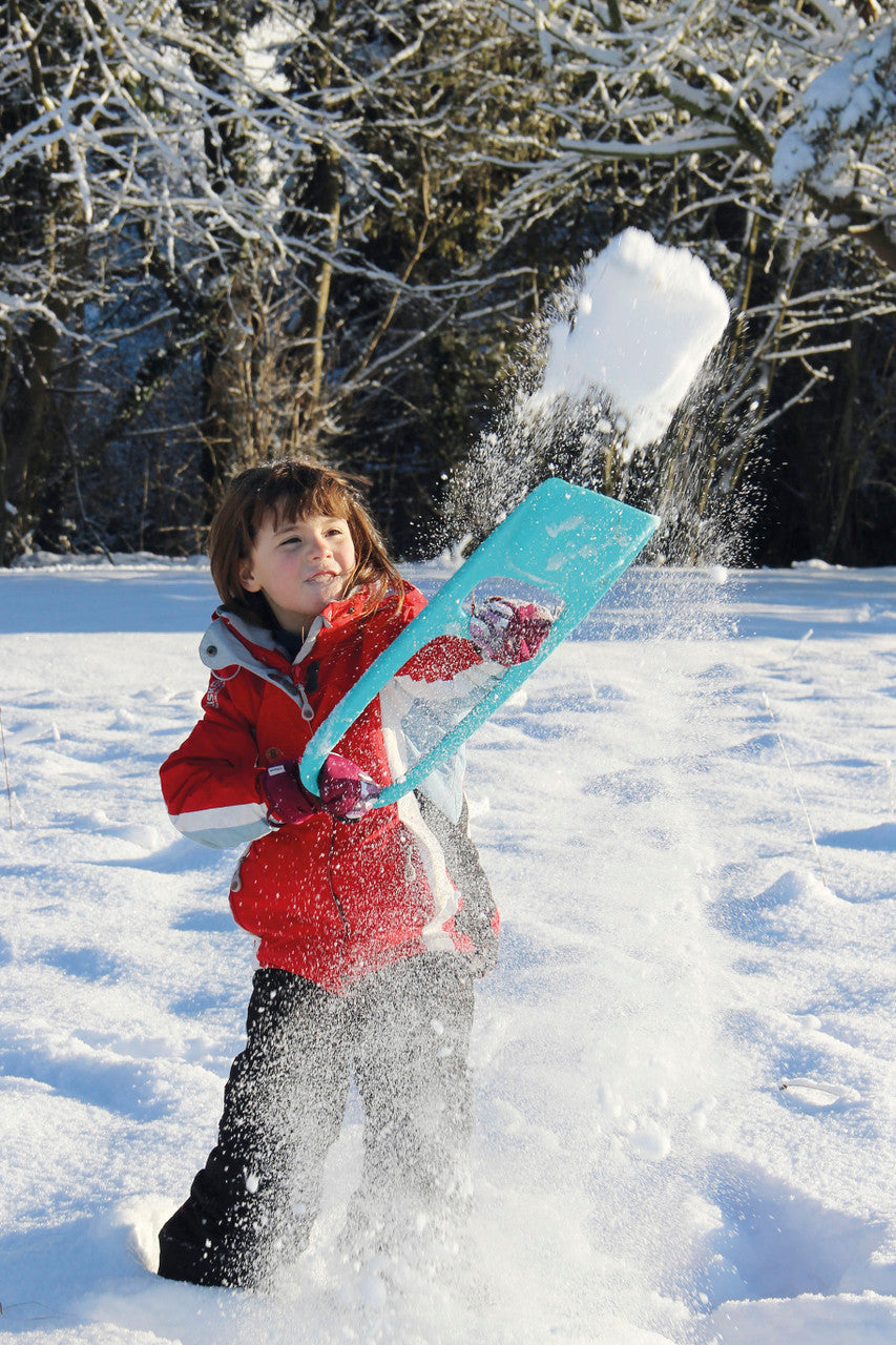 Child playing with turquoise snow shovel tool in winter snow outdoors