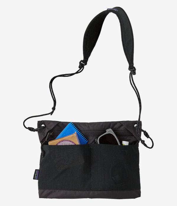 Black crossbody bag with padded shoulder strap and front exterior pockets containing items