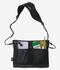 Black crossbody bag with shoulder strap showing front pockets containing phone and cards