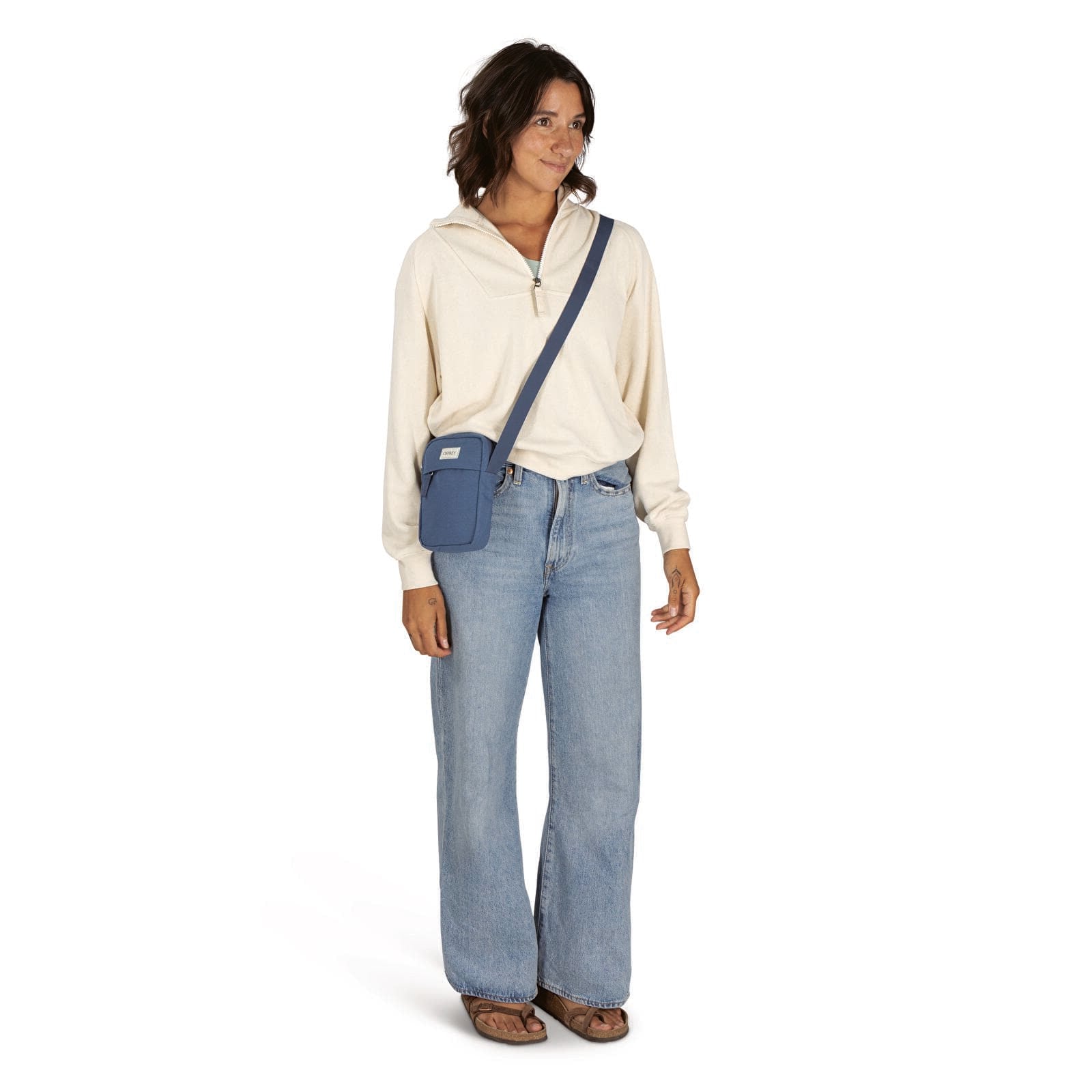 Small crossbody bag in muted blue worn crossbody over cream pullover, front on-model view