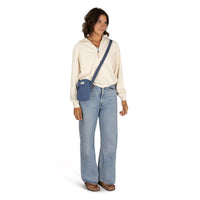 Small crossbody bag in muted blue worn crossbody over cream pullover, front on-model view