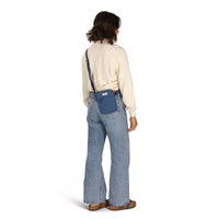 Small blue crossbody bag worn across back on model in cream sweater and flared jeans