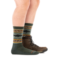 Olive green crew socks with trout fish pattern and striped accents, worn with brown hiking boots