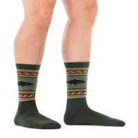 Olive green crew socks with trout fish graphic and multicolor striped band, worn on model