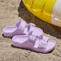 Light purple EVA sandals with two adjustable buckle straps on sandy beach surface