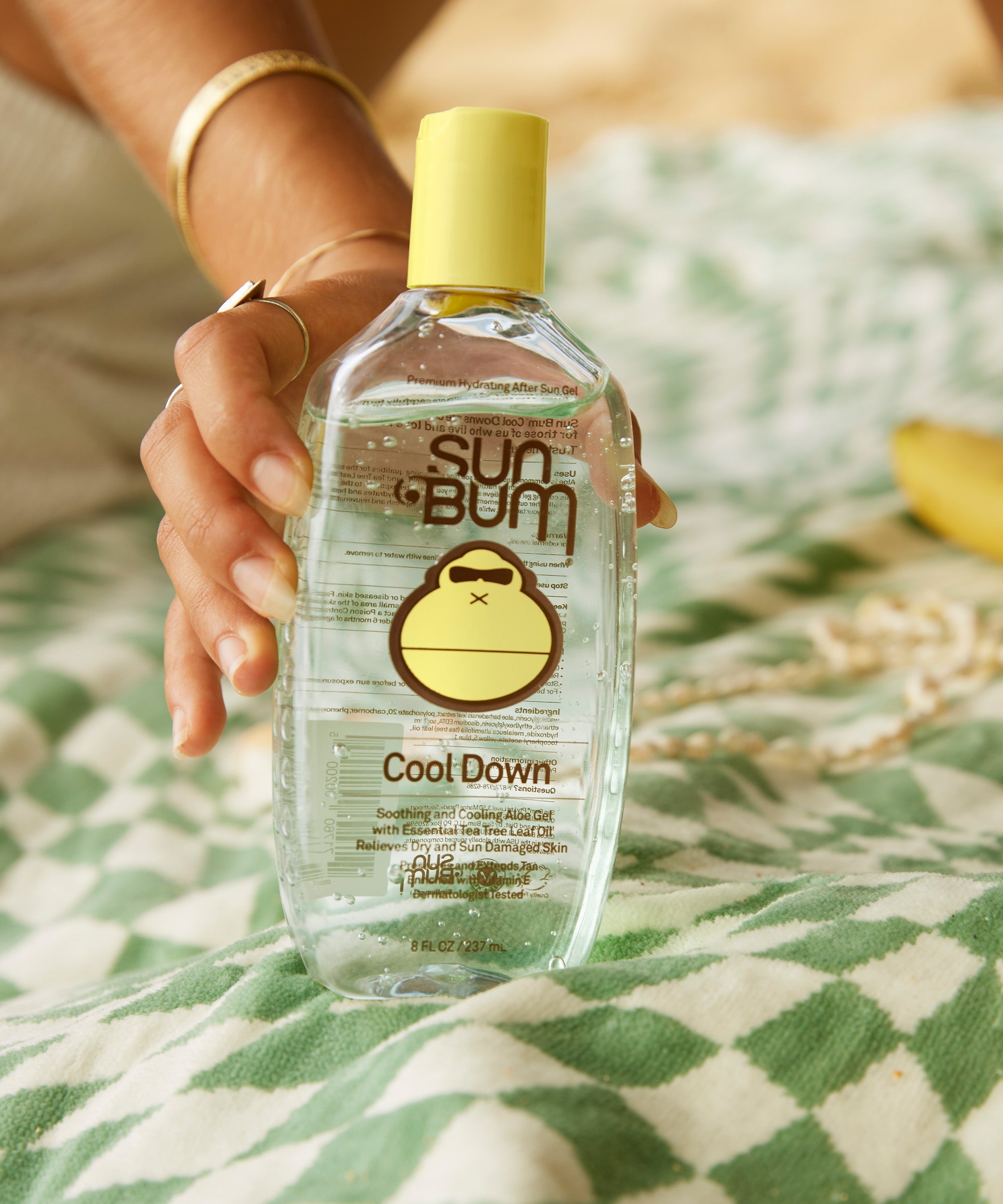 Clear cooling gel bottle with yellow cap held in hand, soothing after-sun skincare product