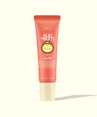 Coral pink tinted lip balm tube with SPF 30 protection, standing upright against cream background