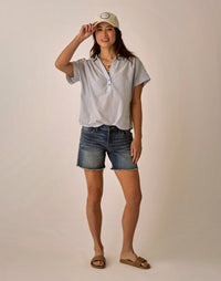 Woman wearing light blue pinstriped short-sleeve button-up top with denim shorts