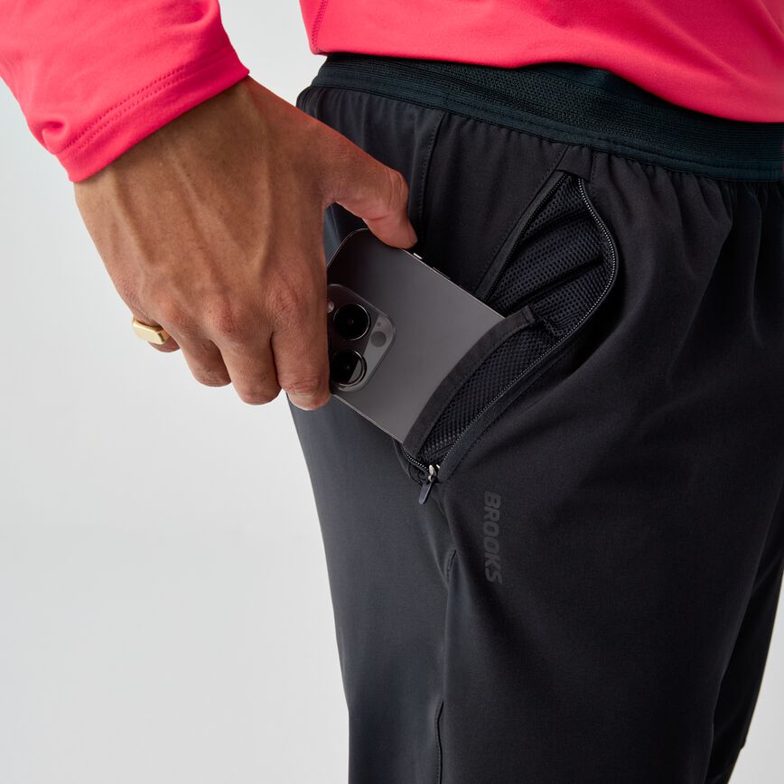 Black athletic pants with zippered side pocket, person inserting phone into pocket