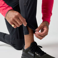 Black athletic pants with ankle zip detail, shown on kneeling person adjusting cuff