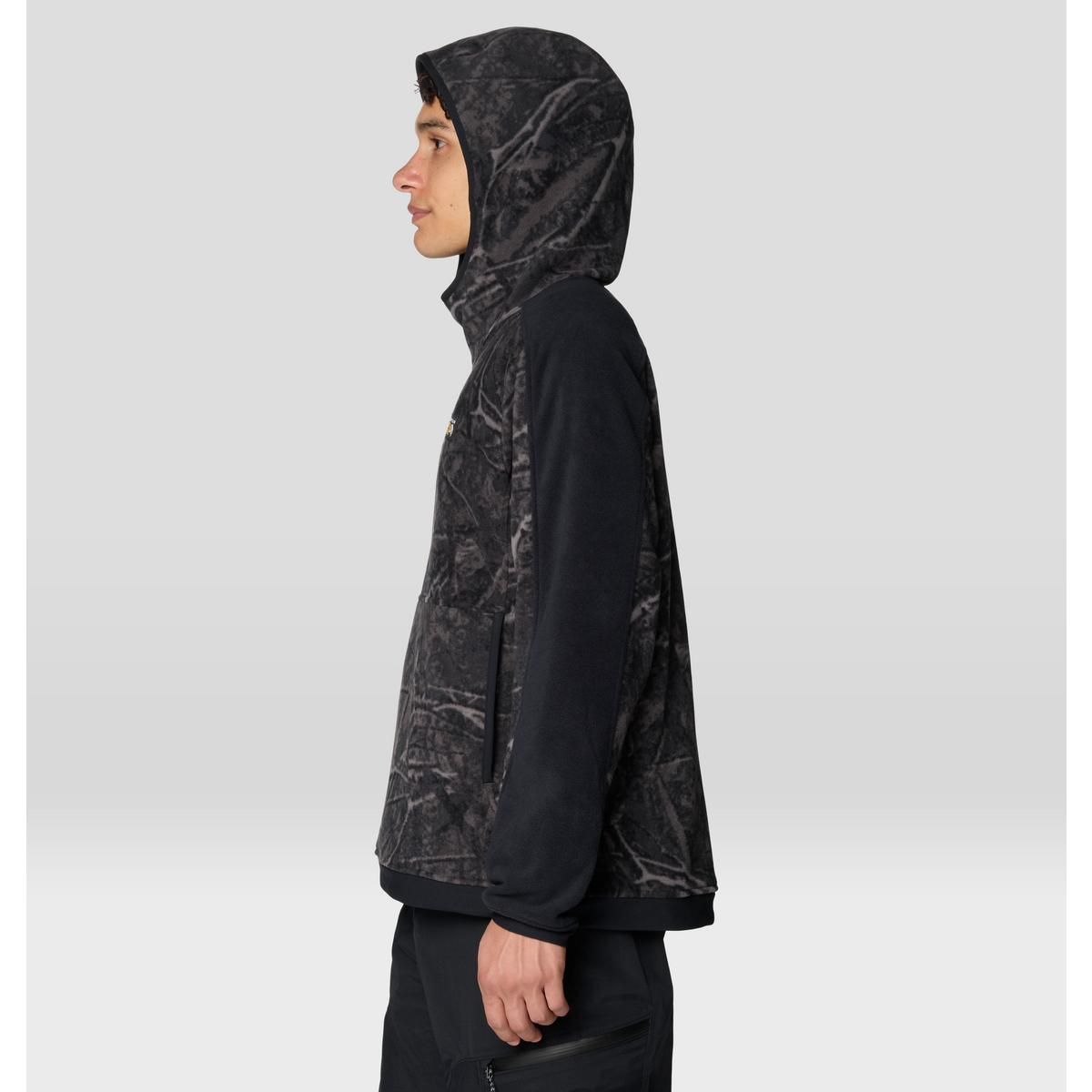 Men's fleece hoodie with tree camo print body, solid black sleeves, side view on model