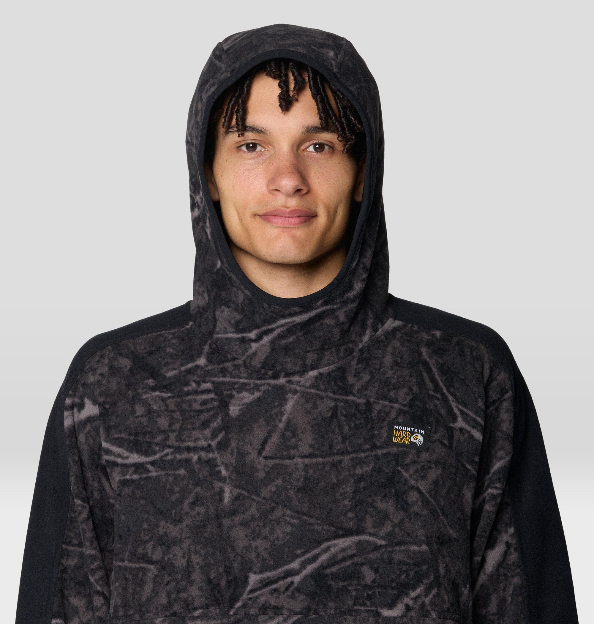 Men's fleece pullover hoodie with abstract dark treecover print, hood up, close-up front view