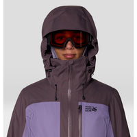 Women's hooded ski jacket close-up with Oakley goggles, two-tone purple colorblock design, adjustable hood