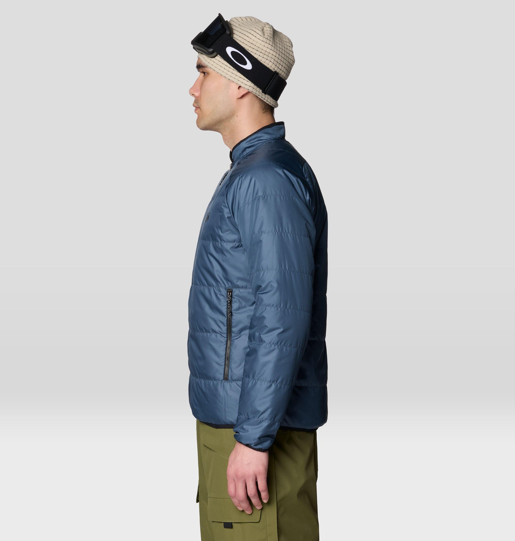 Men's insulated puffer jacket in steel blue, side view, with zip pocket and ski goggles on beanie