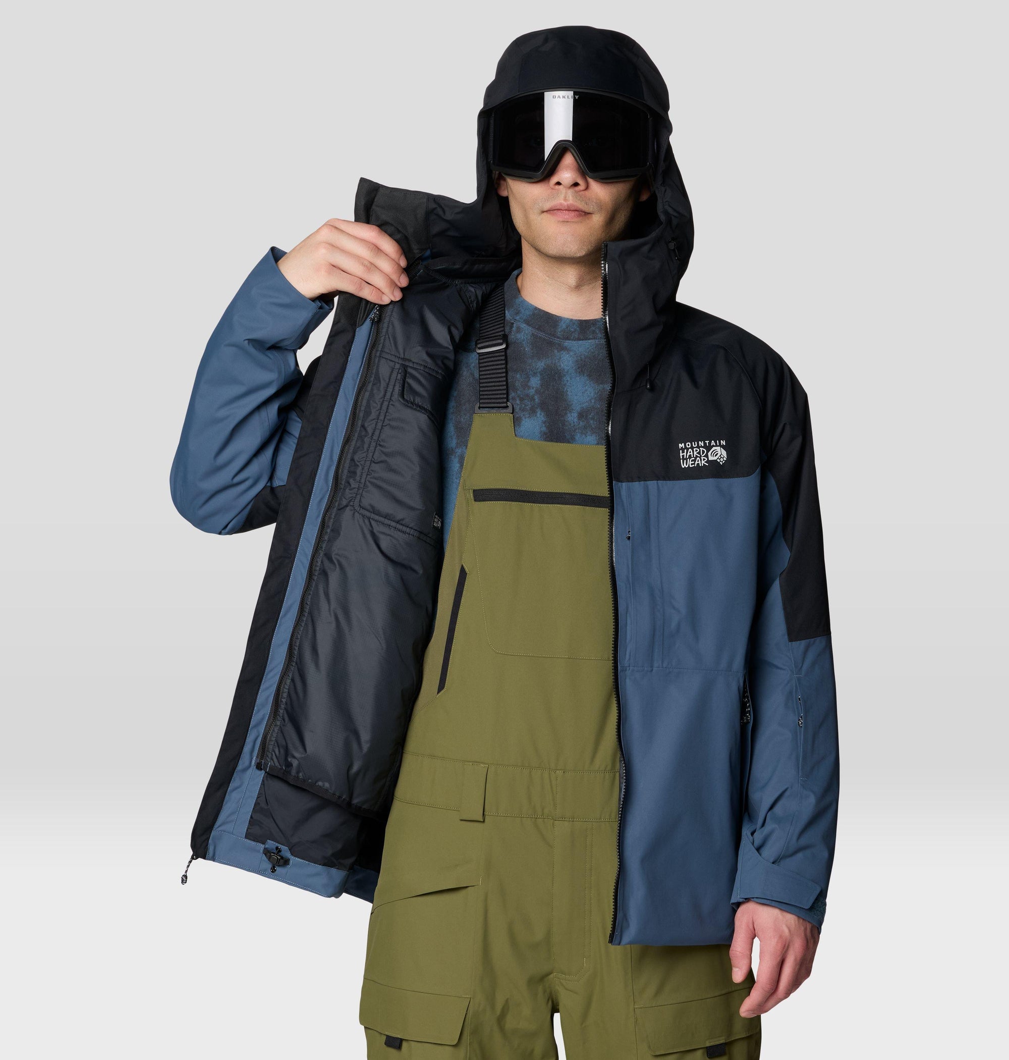 Men's ski jacket open to show insulated interior, worn with ski goggles and olive bibs