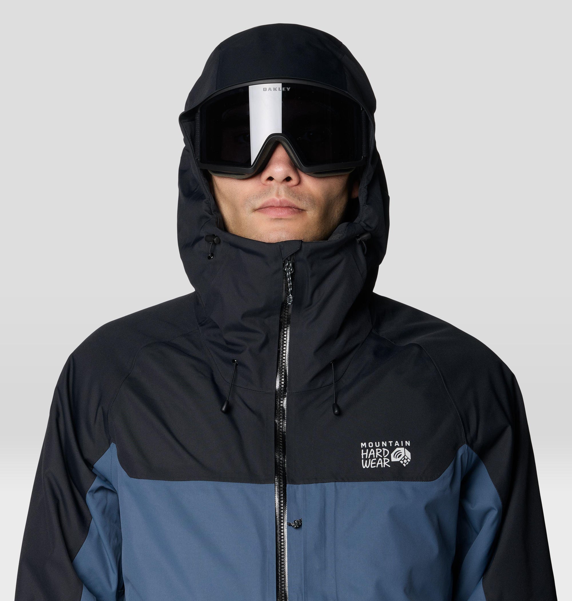 Men's hooded ski jacket with colorblock design, worn with Oakley goggles, close-up front view