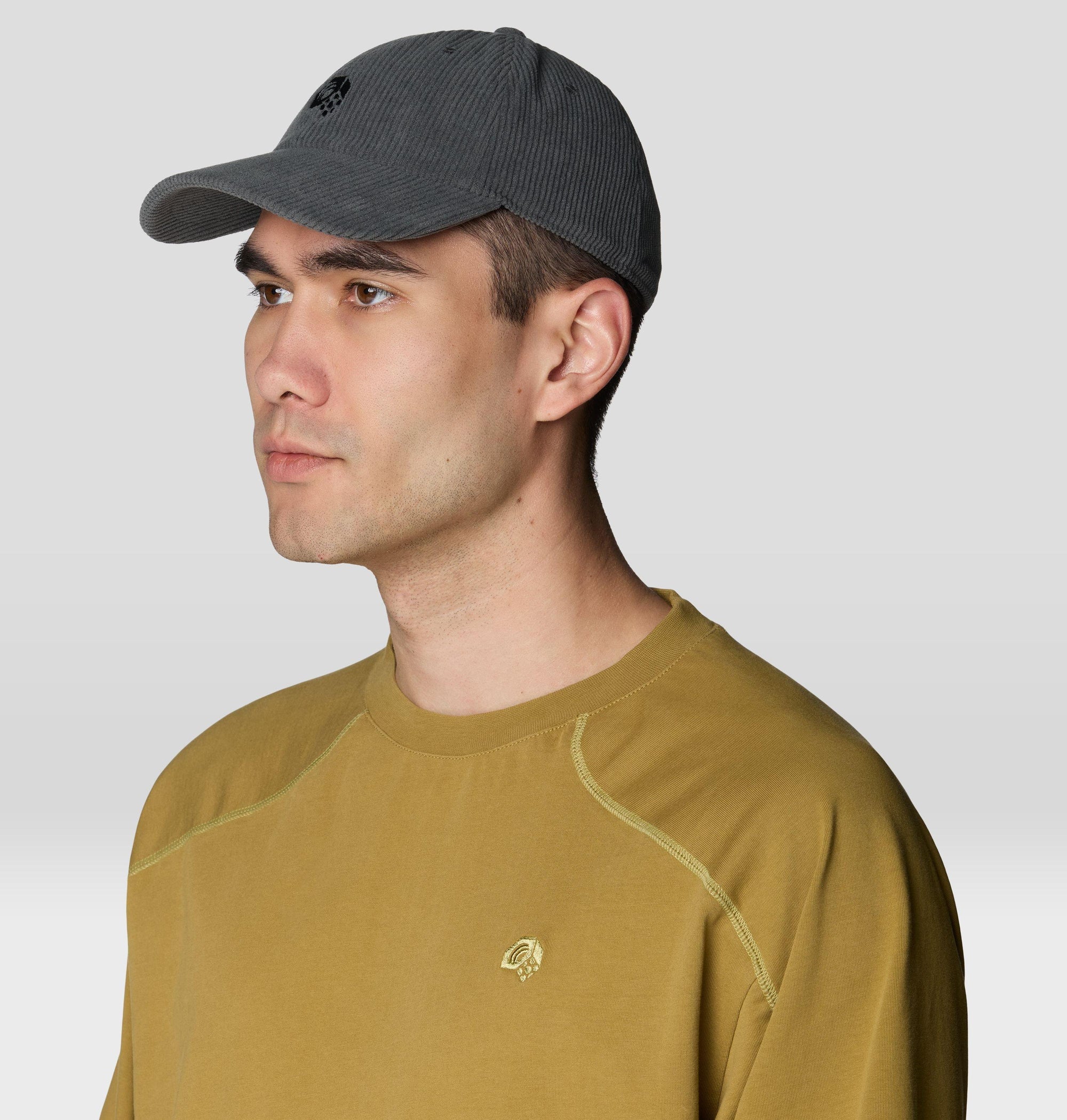 Dark gray corduroy baseball cap with small logo, worn on male model, side angle view