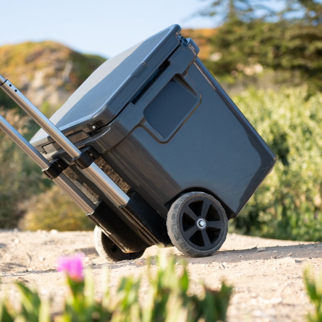 Navy blue wheeled cooler with retractable handle positioned on outdoor ground with natural background