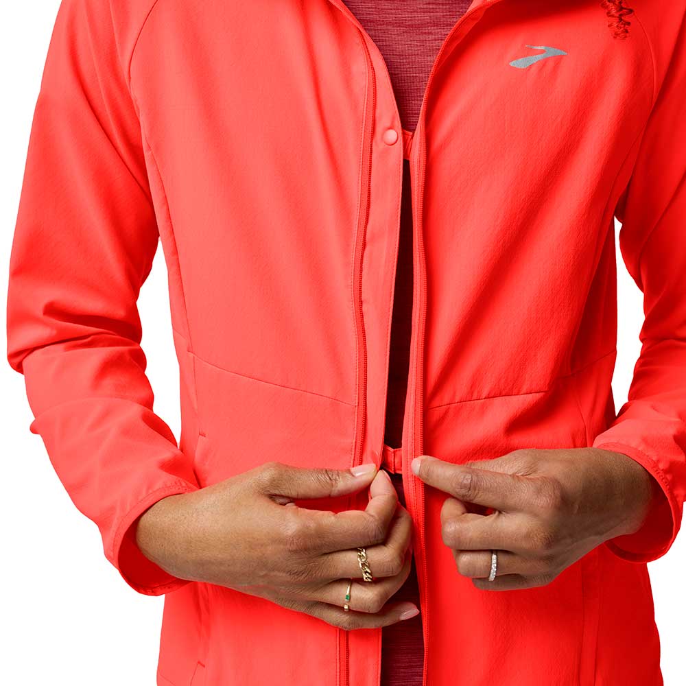 Bright coral running jacket with full zip closure worn by person, hands positioned at zipper