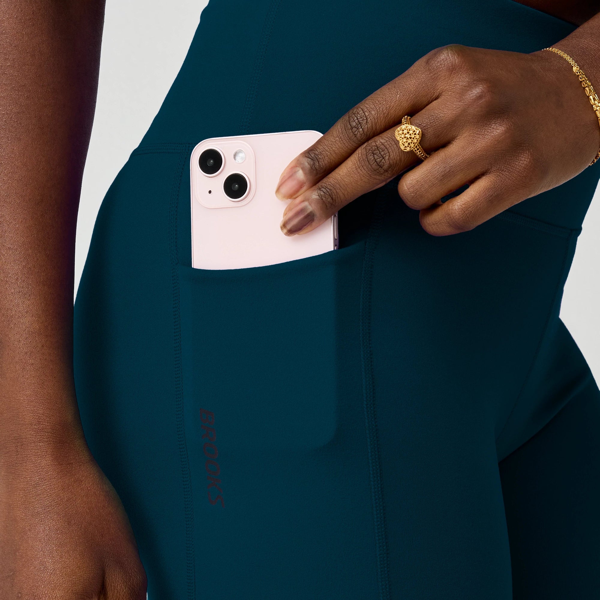 Dark teal athletic shorts with side pocket, worn by model putting phone in pocket