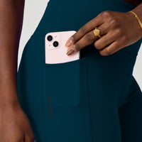 Dark teal athletic shorts with side pocket, worn by model putting phone in pocket