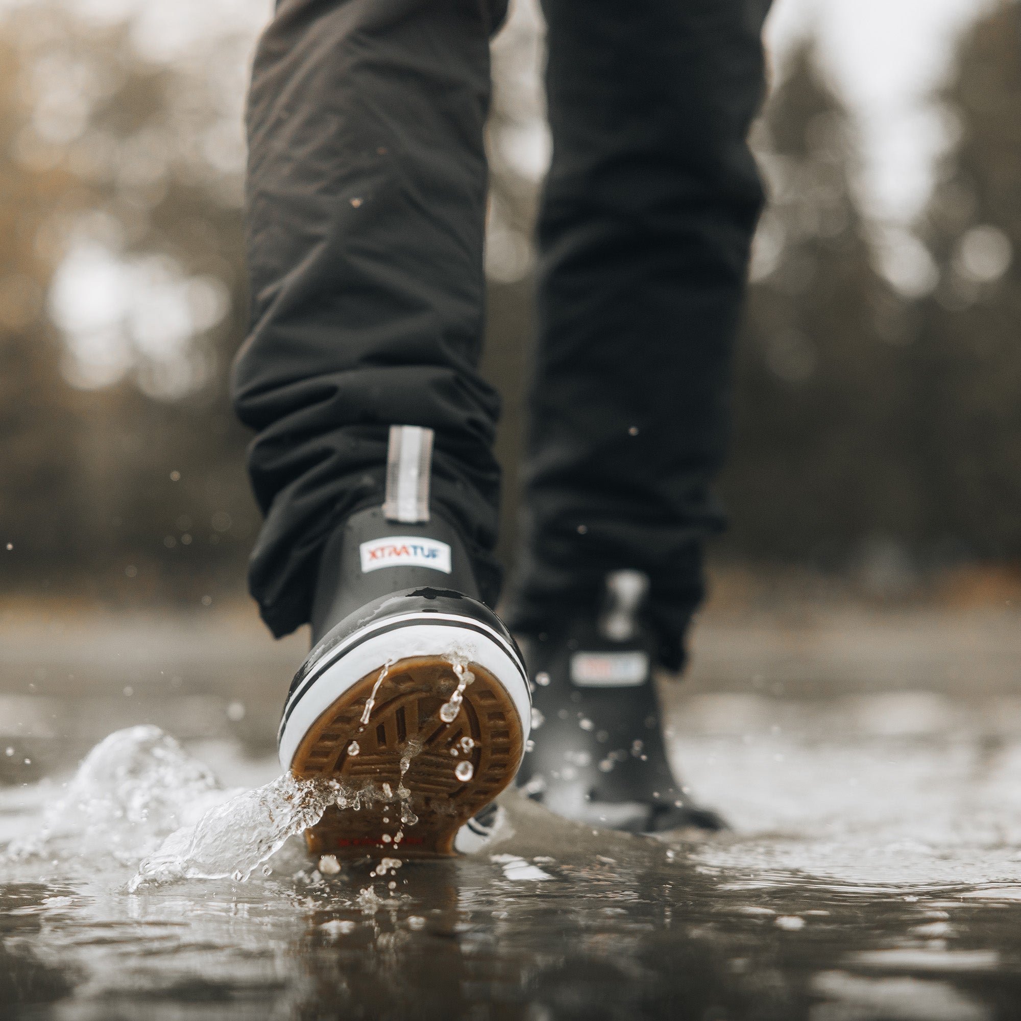 Black ankle deck boots splashing through a water puddle, showing rubber sole and grip tread