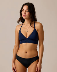 Women's reversible bikini bottom in black, front view on model with navy halter top