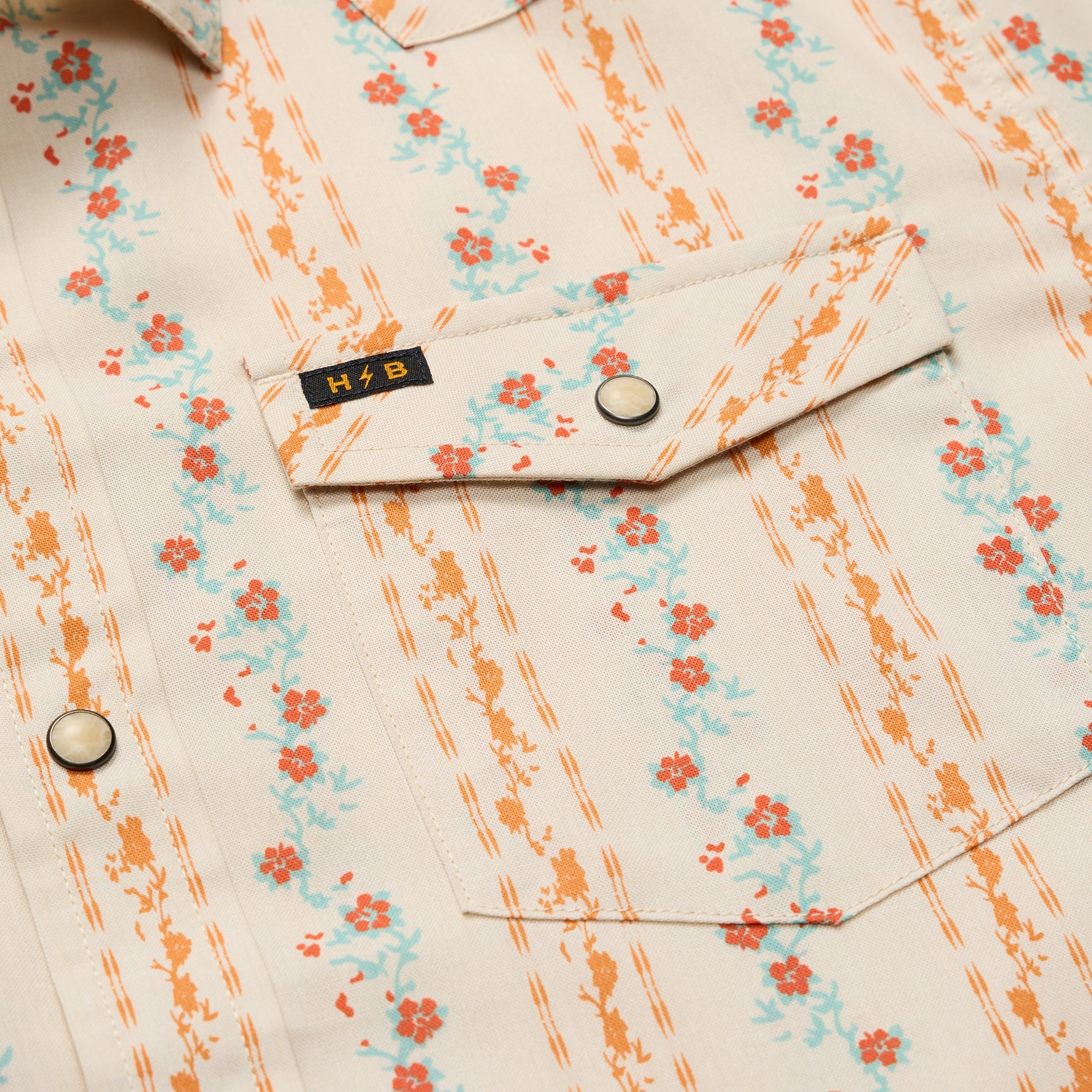 Close-up detail of floral print snap shirt showing chest pocket, snap button, and brand label